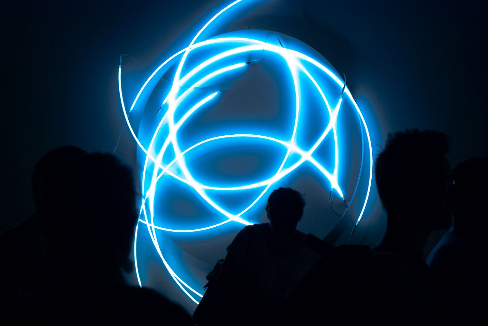 blue-neon-semicircles-crossing-each-other-in-a-dark-gallery-space-where-shades-of-people-are-passing-by